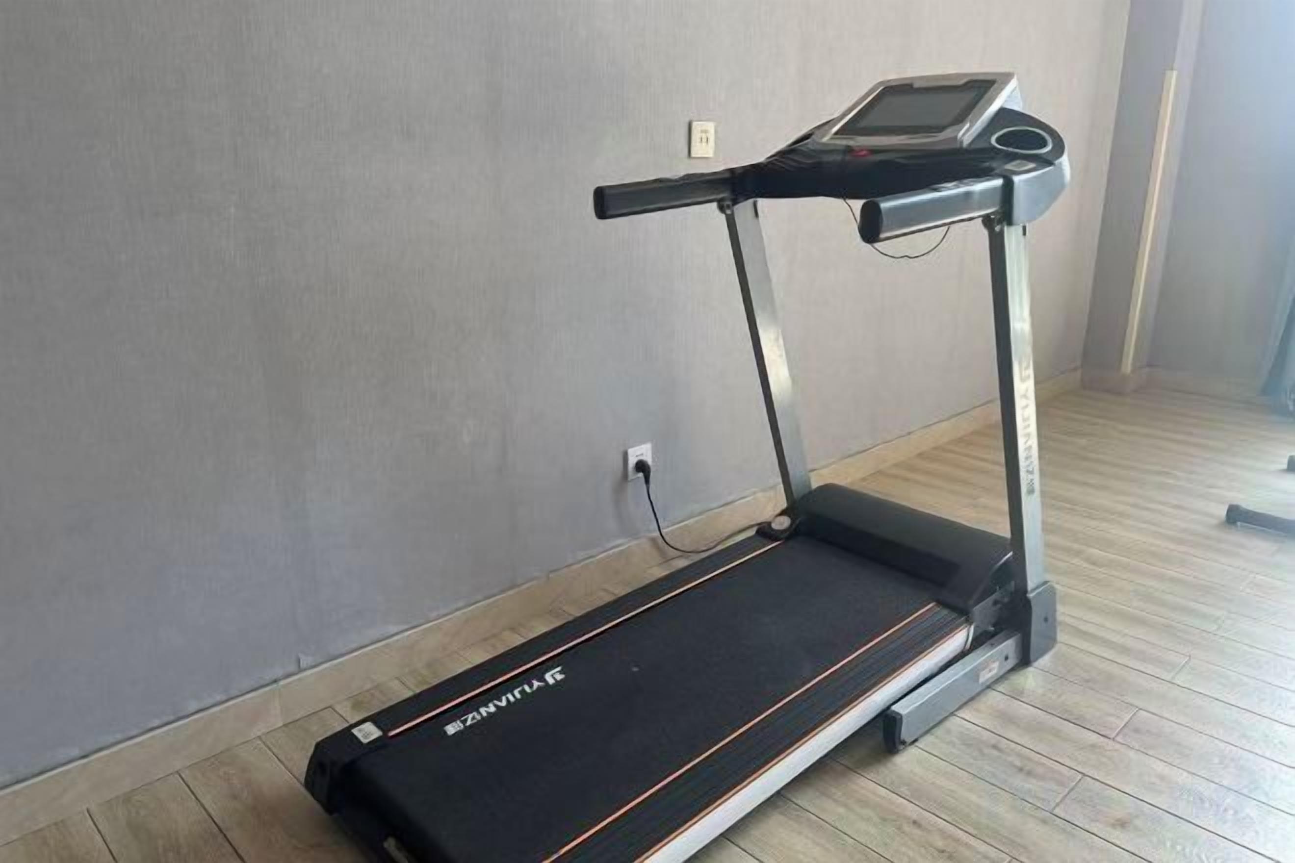 A treadmill in a room with a wooden floor and a plain wall.
