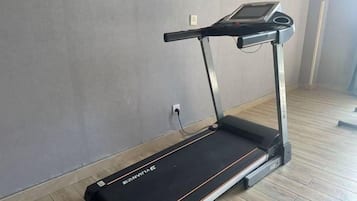 A treadmill in a room with a wooden floor and a plain wall.