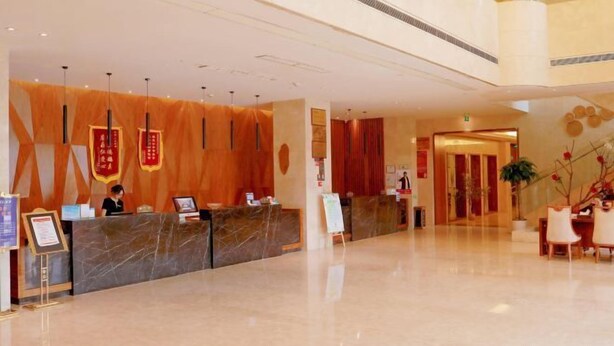 A hotel lobby with a marble reception desk, a receptionist, and a seating area with a plant. - Lijing Hotel (Ningbo)