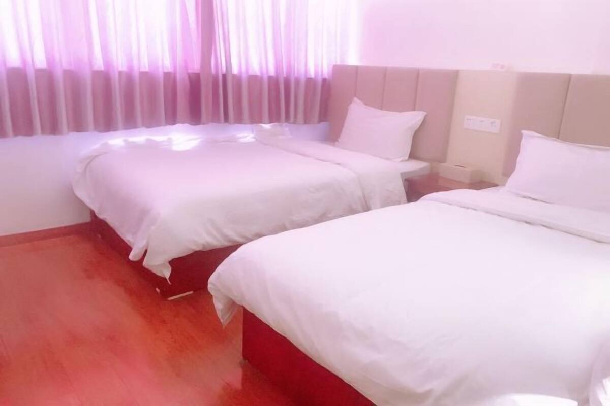 A hotel room with two beds, a red carpet, and a window with sheer curtains.