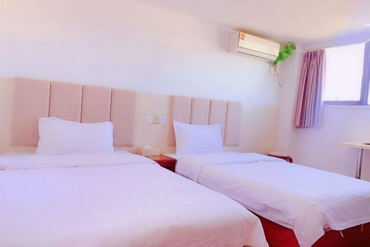 A hotel room with two beds, a bedside table, an air conditioning unit, and a window with curtains.