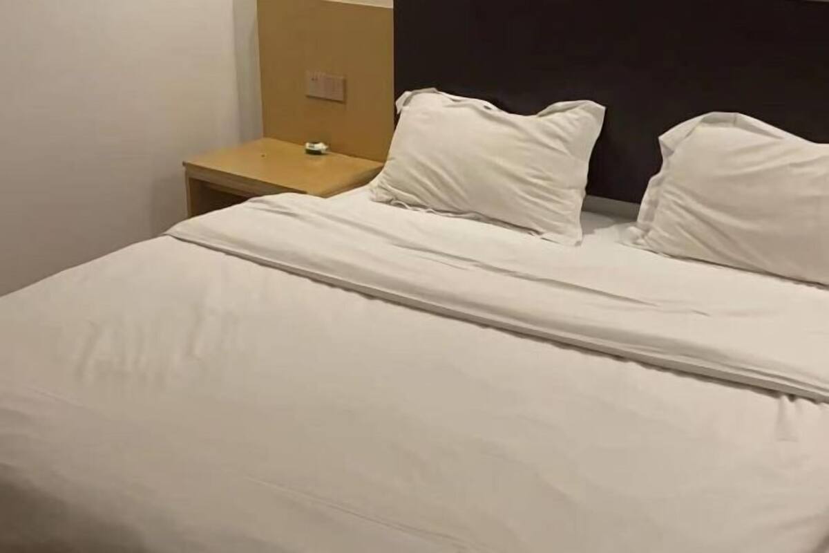 A bed with white bedding, a small wooden nightstand with a lamp, and a dark headboard.