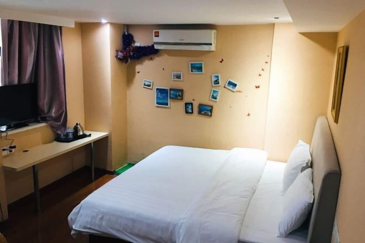 A hotel room with a bed, a desk, a television, and a wall decorated with photos.