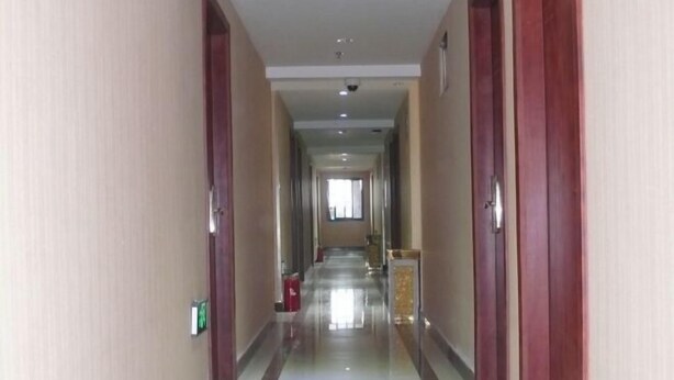 A hotel corridor with a shiny floor, wooden doors, and a visible emergency exit sign. - Yaocheng Hotel (Shanghai)