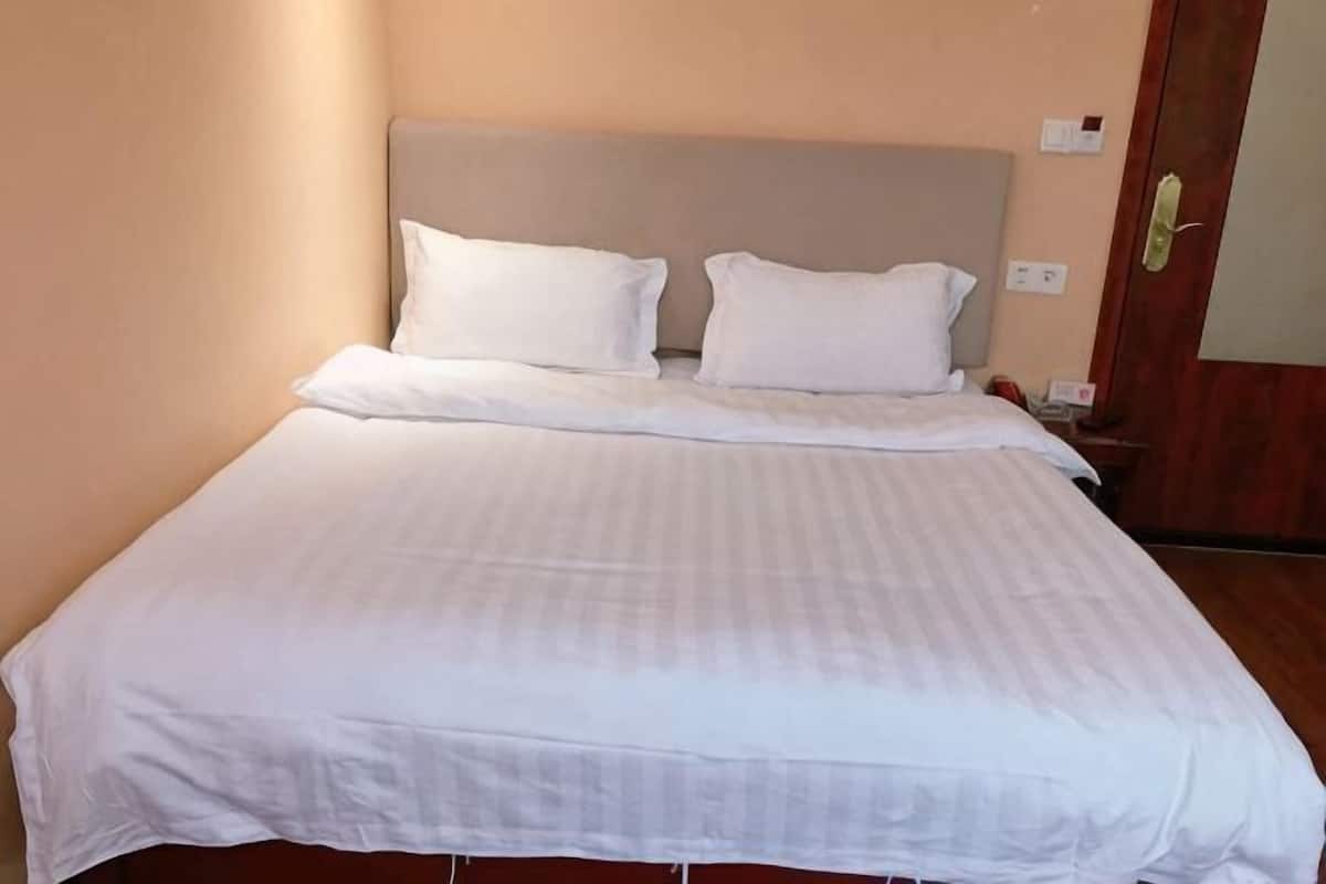 A neatly made bed with white linens and a headboard, a wooden door, and a wall switch.