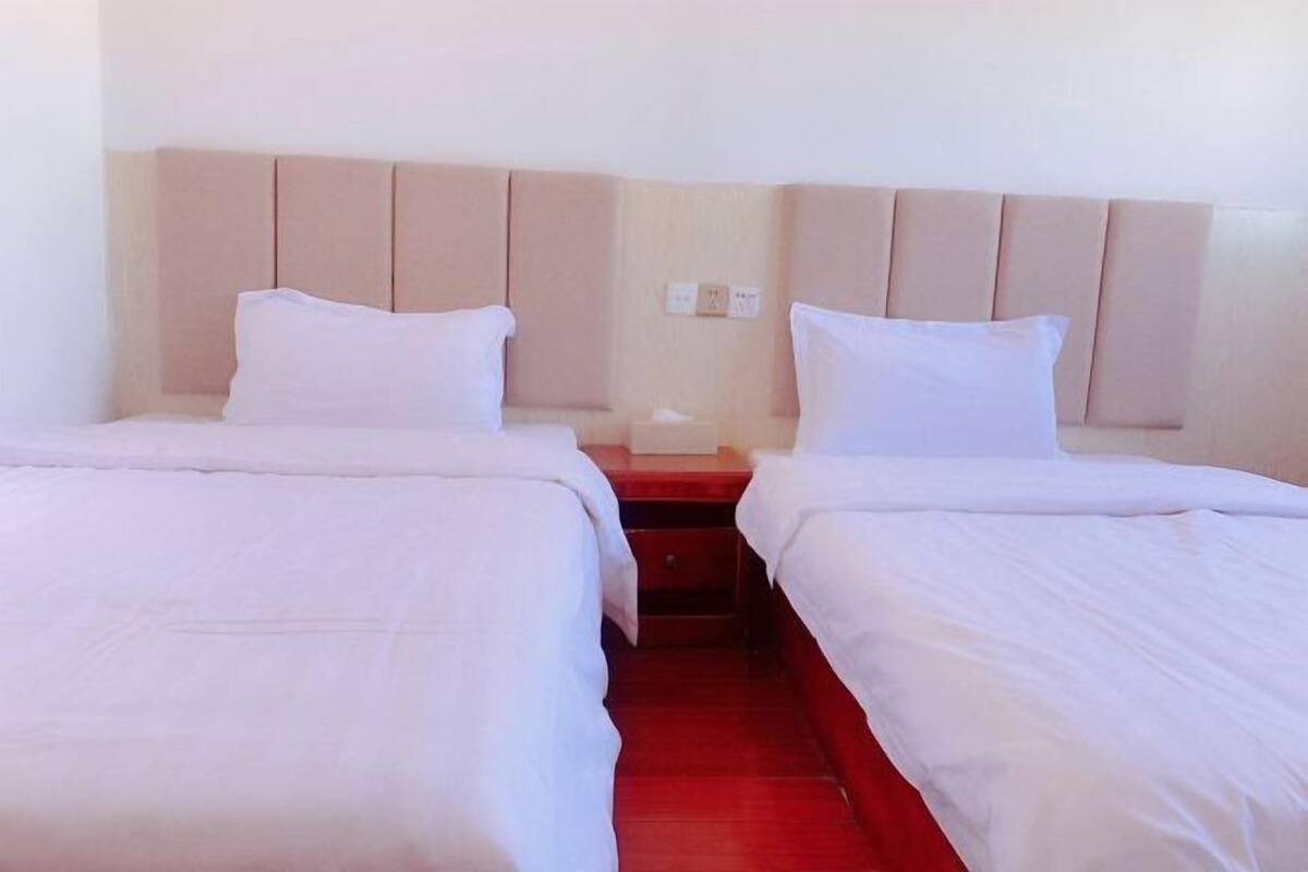 A hotel room with two beds, a red carpet, and a wooden nightstand with a lamp.