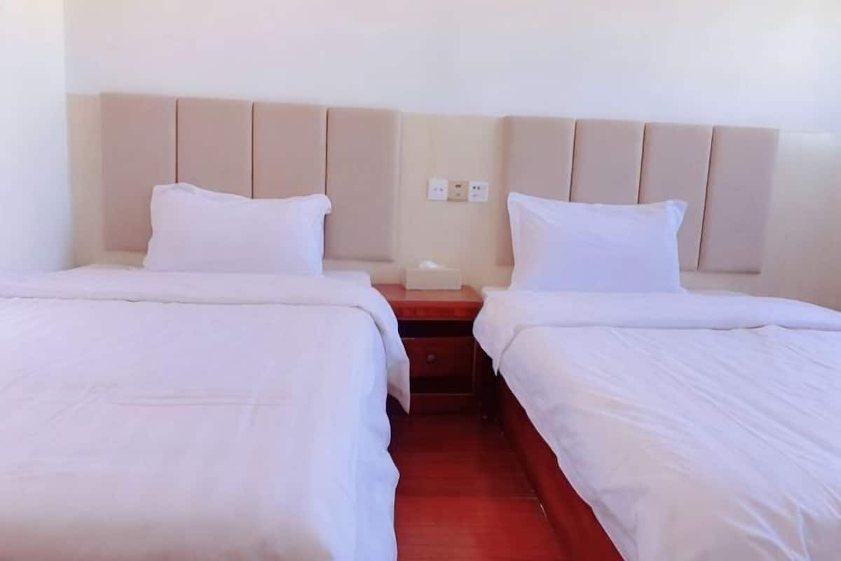 A hotel room with two beds, a nightstand, and a wall-mounted light switch.