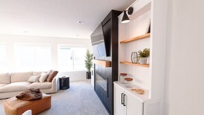 En moderne stue med sofa, sofabord og fjernsyn. Reoler med pynteting og en plante.