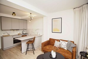 A modern kitchen with a marble countertop, a dining area with a white table and two chairs, a brown leather sofa with cushions, and a framed artwork on the wall. - Close to the beach, free sauna and pool - Strandresidenz Brandenburg FeWo 30 - House (Göhren)