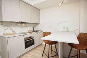 A modern kitchen with white cabinets, a built-in oven, a sink, and a dining area with two stools.