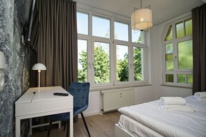 A hotel room with a bed, a desk, a chair, and large windows offering a view of greenery. - Close to the beach, sauna + swimming pool free of charge - Strandresidenz Brandenburg FeWo 30 - House (Göhren)