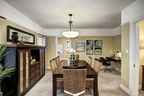 A dining area with a wooden table, wicker chairs, a chandelier, and artwork on the walls.