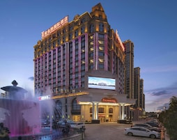 A multi-story hotel with a prominent entrance, a large digital display, and a fountain in the foreground.