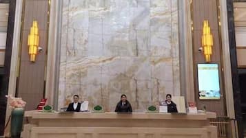 A reception desk with three individuals seated behind it, a marble wall in the background, and two wall-mounted light fixtures.