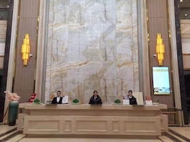 Un mostrador de recepción con tres personas sentadas detrás, una pared de mármol al fondo y dos lámparas fijadas a la pared.