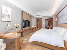 Une chambre d’hôtel avec un grand lit, un bureau avec une lampe, un vase de fleurs, une télévision et un tableau au mur.