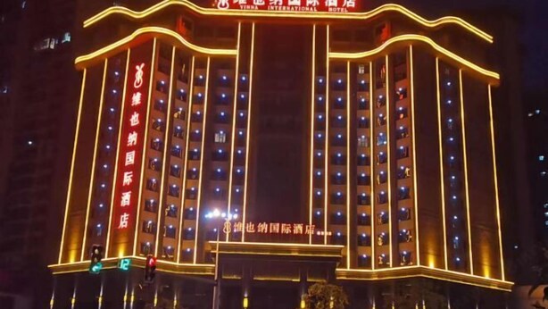 Un hotel de varios pisos, iluminado con luz cálida, y con un cartel llamativo en la entrada.