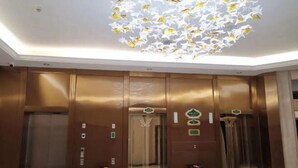 Interior de un ascensor con paredes metálicas, techo reflectante y puerta con un letrero verde.