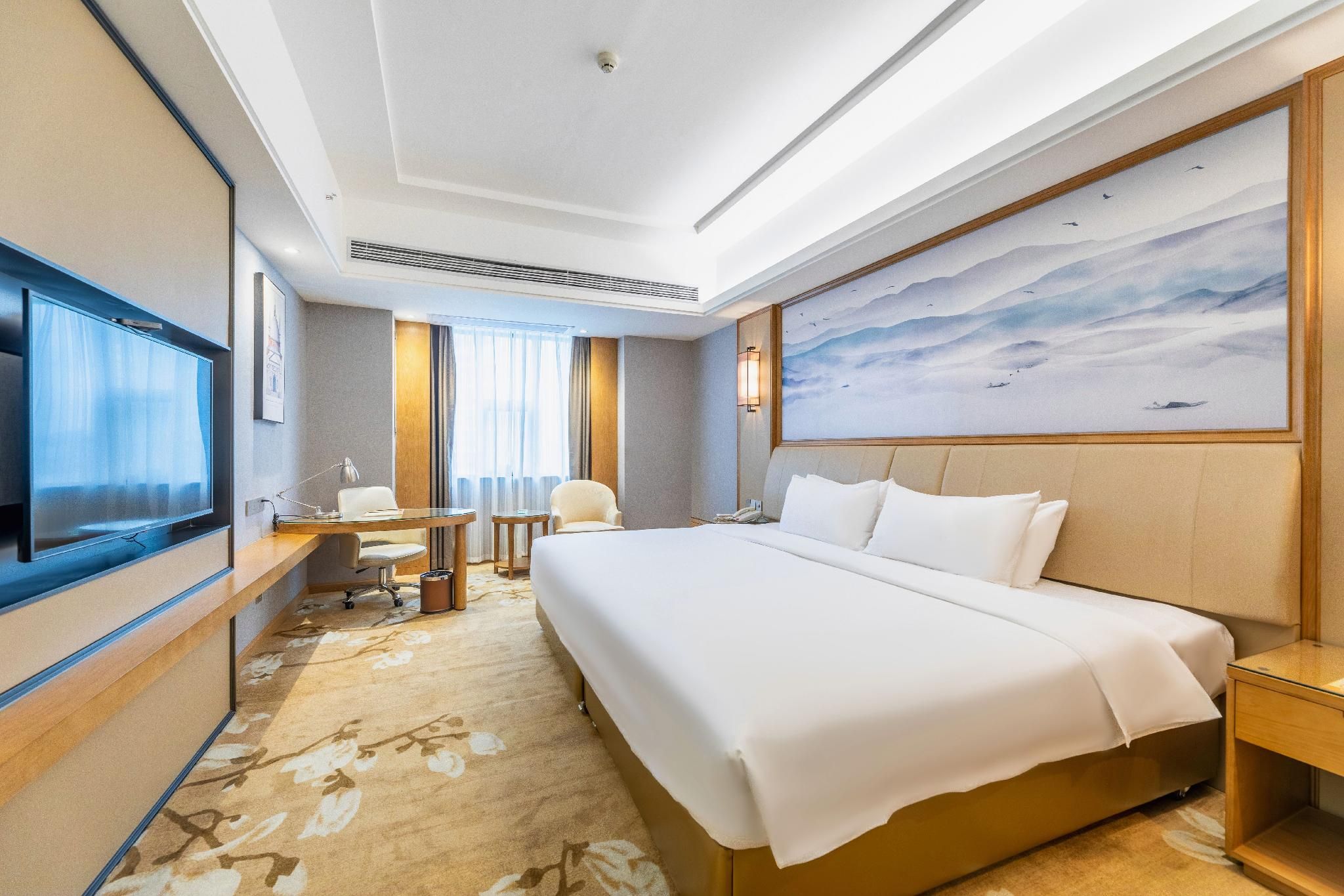 Ein Hotelzimmer mit einem großen Bett, einem Schreibtisch, einem Sessel, einem Fernseher und einem Gemälde an der Wand.