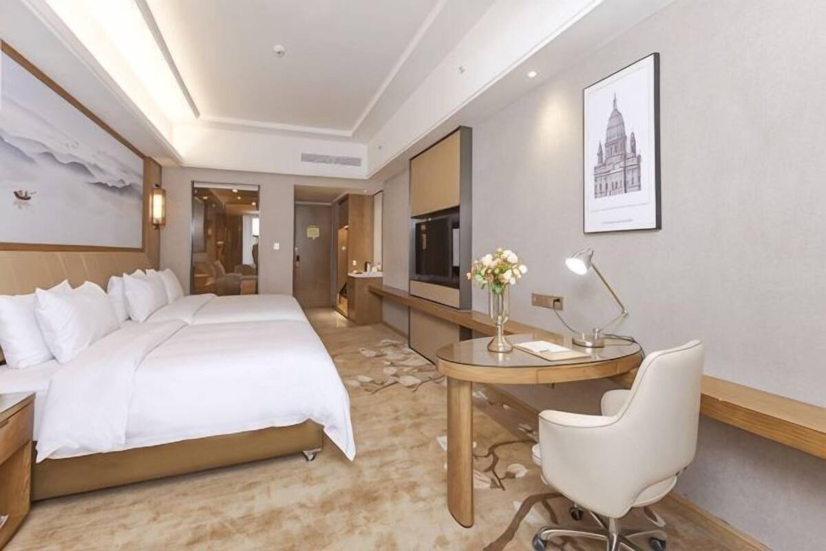 A hotel room with a large bed, a desk with a chair, a mirror, and artwork on the walls.