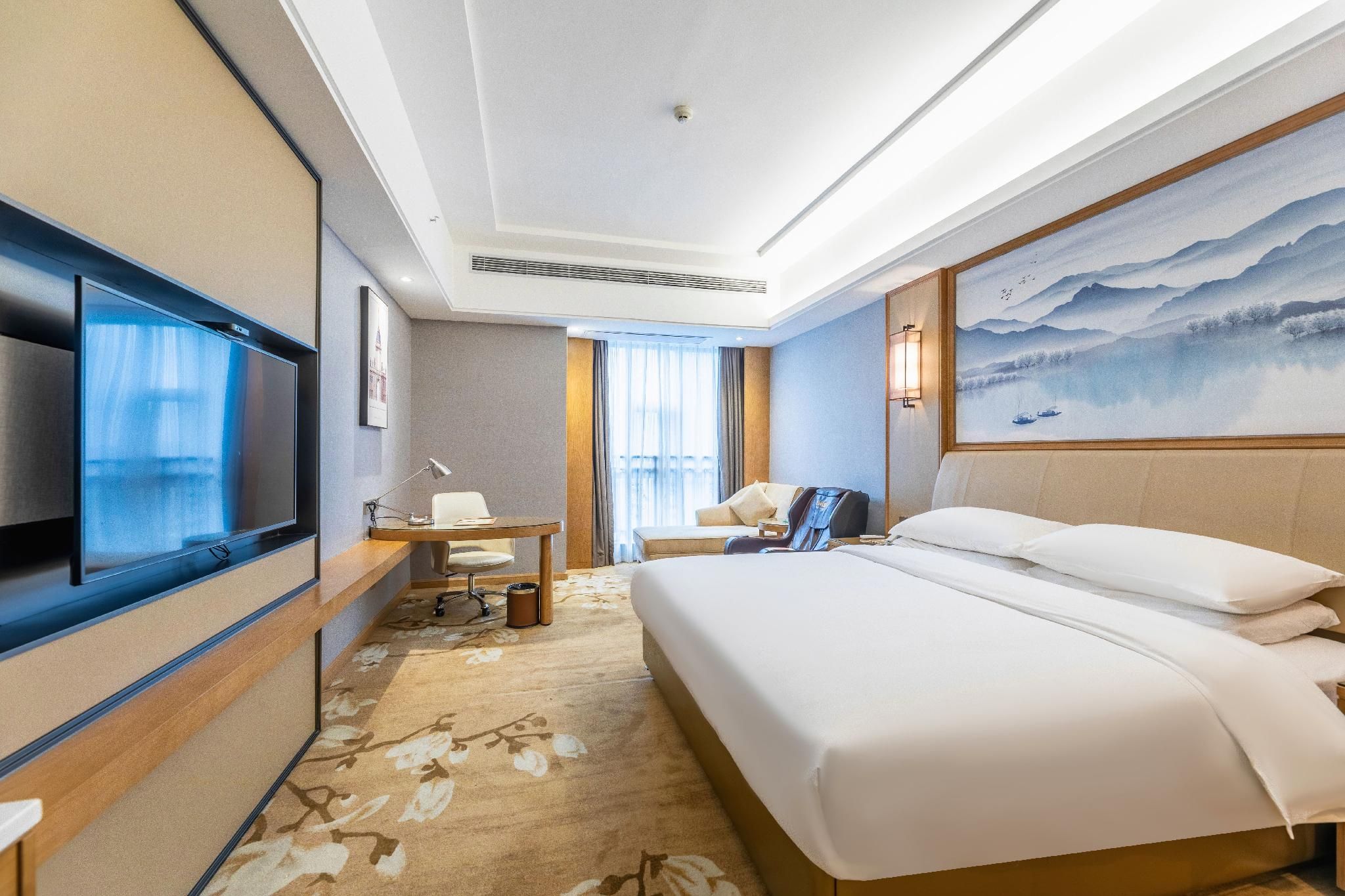 A hotel room with a bed, desk, chair, television, and a painting on the wall.