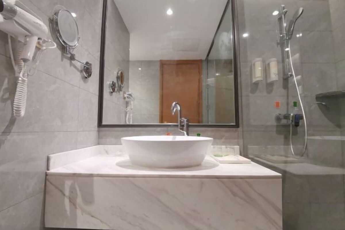 A modern bathroom with a large mirror, a white sink, and a glass-enclosed shower.