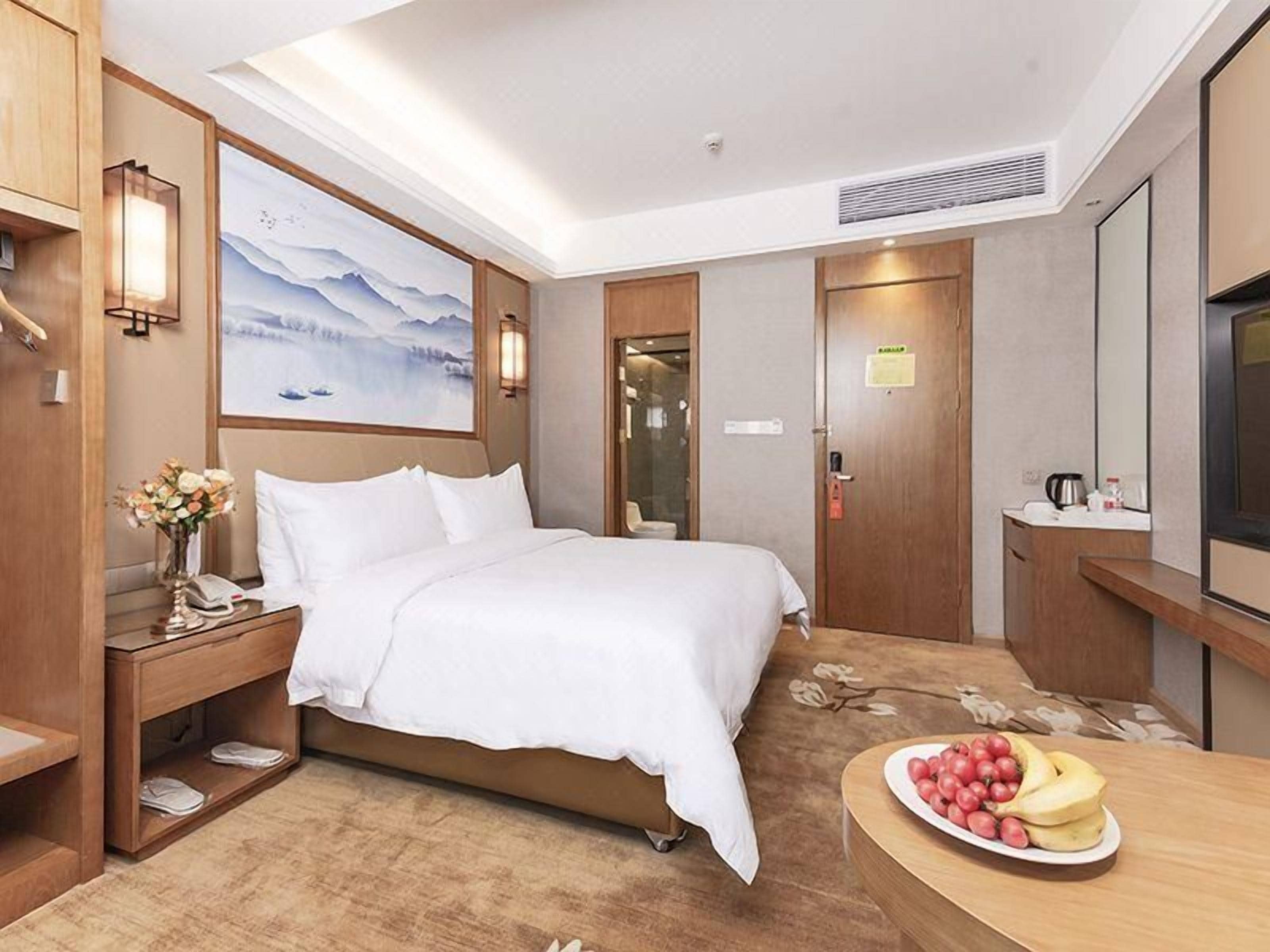 Una habitación de hotel con cama, mesita de noche, lámpara y un cuadro en la pared.