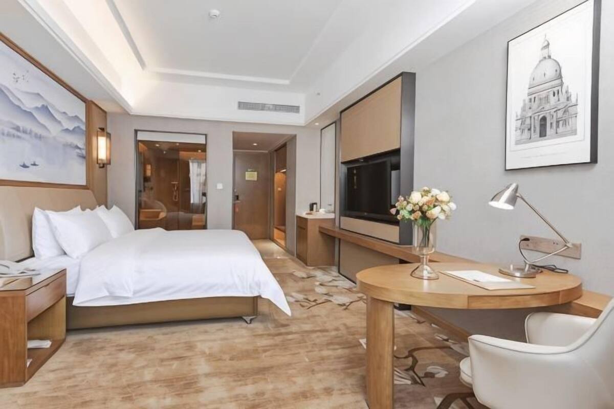 A hotel room with a bed, desk, chair, TV, and artwork on the walls.
