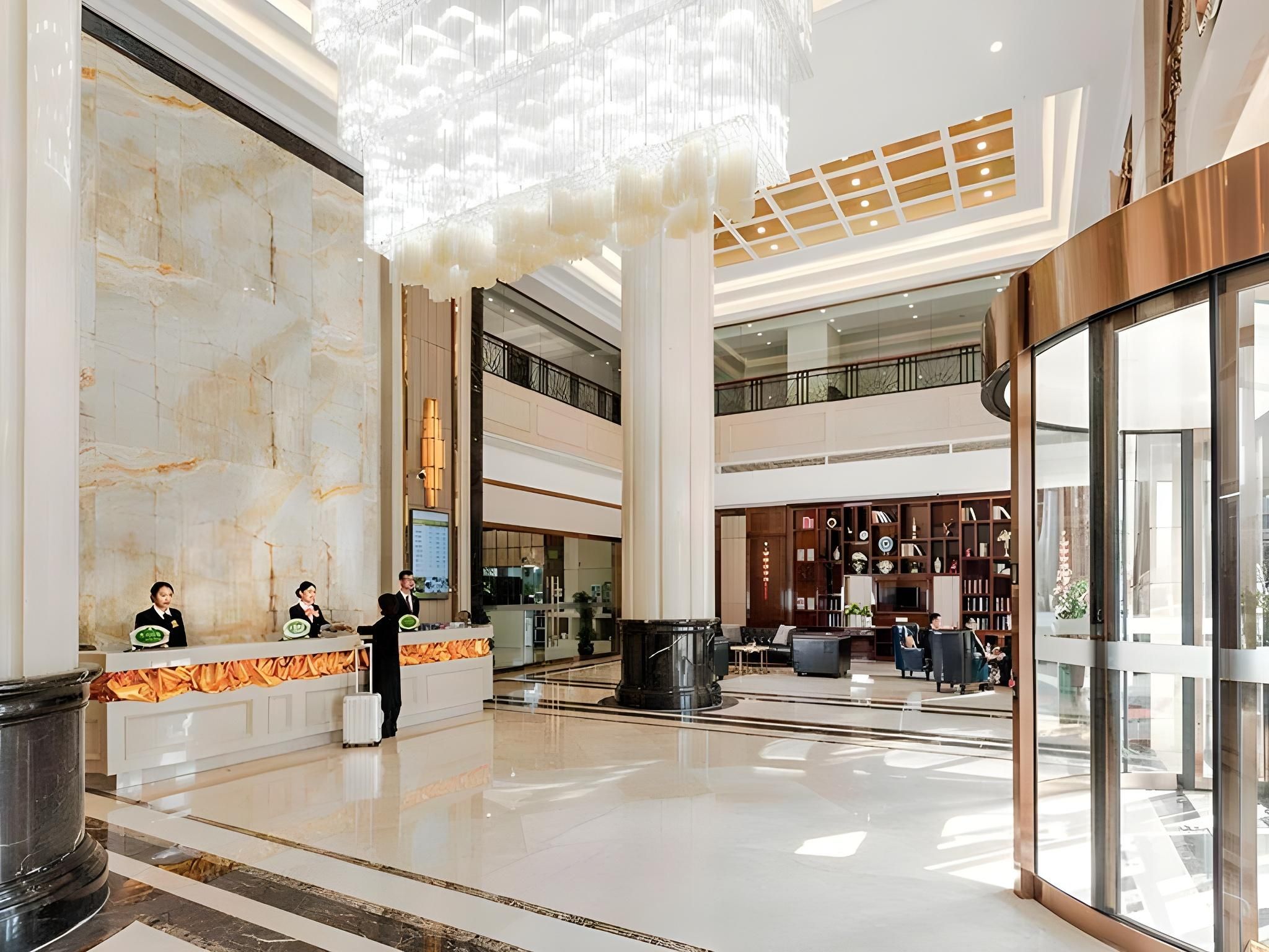 A spacious lobby with a marble reception desk, a large chandelier, and a multi-level atrium with a glass railing.