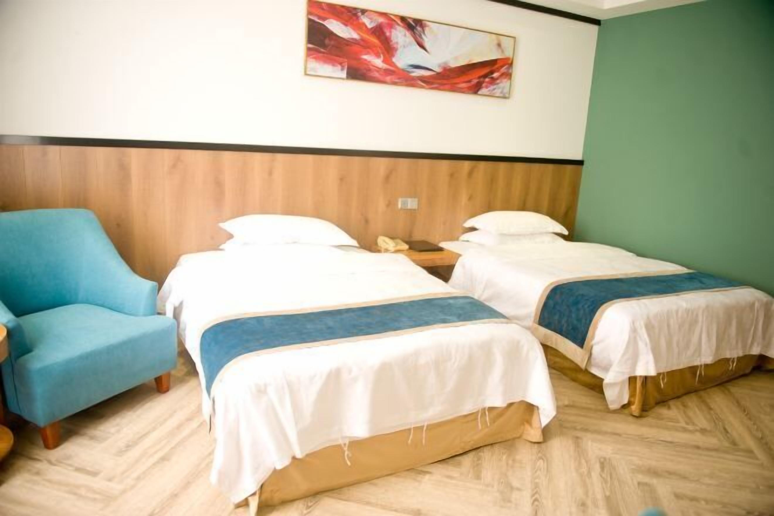 A hotel room with two beds, a blue armchair, and a wooden headboard.