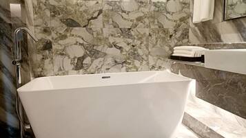 A modern bathroom with a freestanding bathtub, marble walls, and a large mirror.