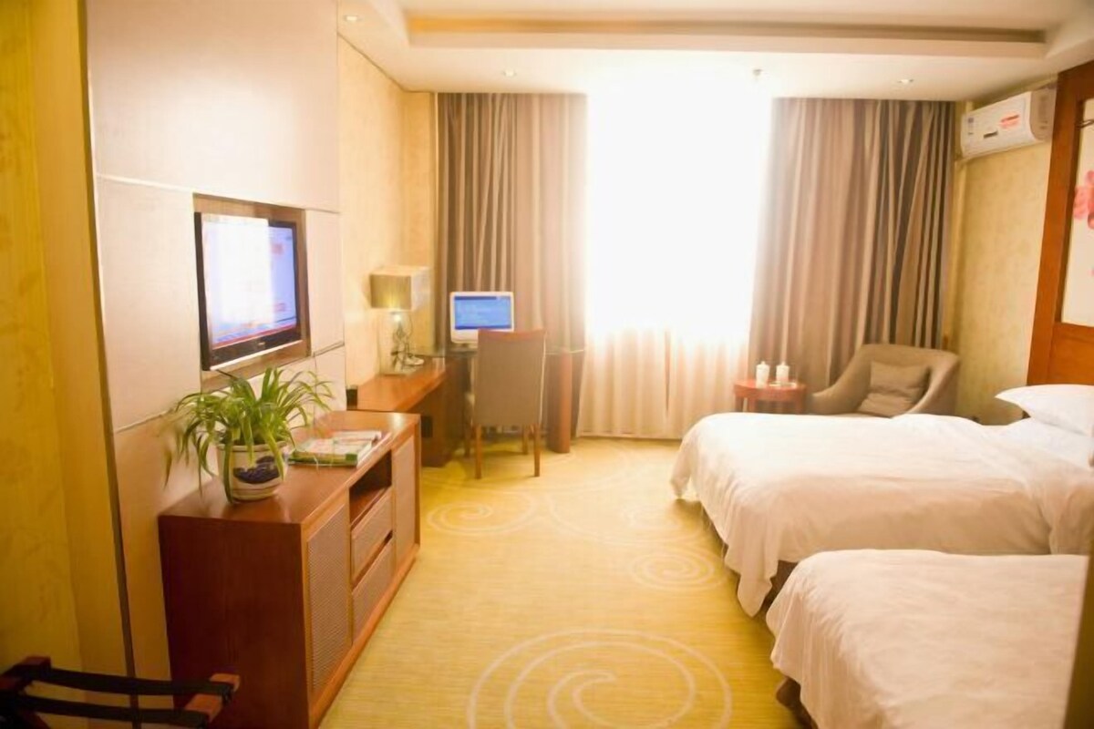 A hotel room with two beds, a desk with a computer, a TV, and a plant.