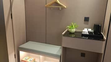 A compact hotel room with a built-in shelf containing slippers and a small potted plant.
