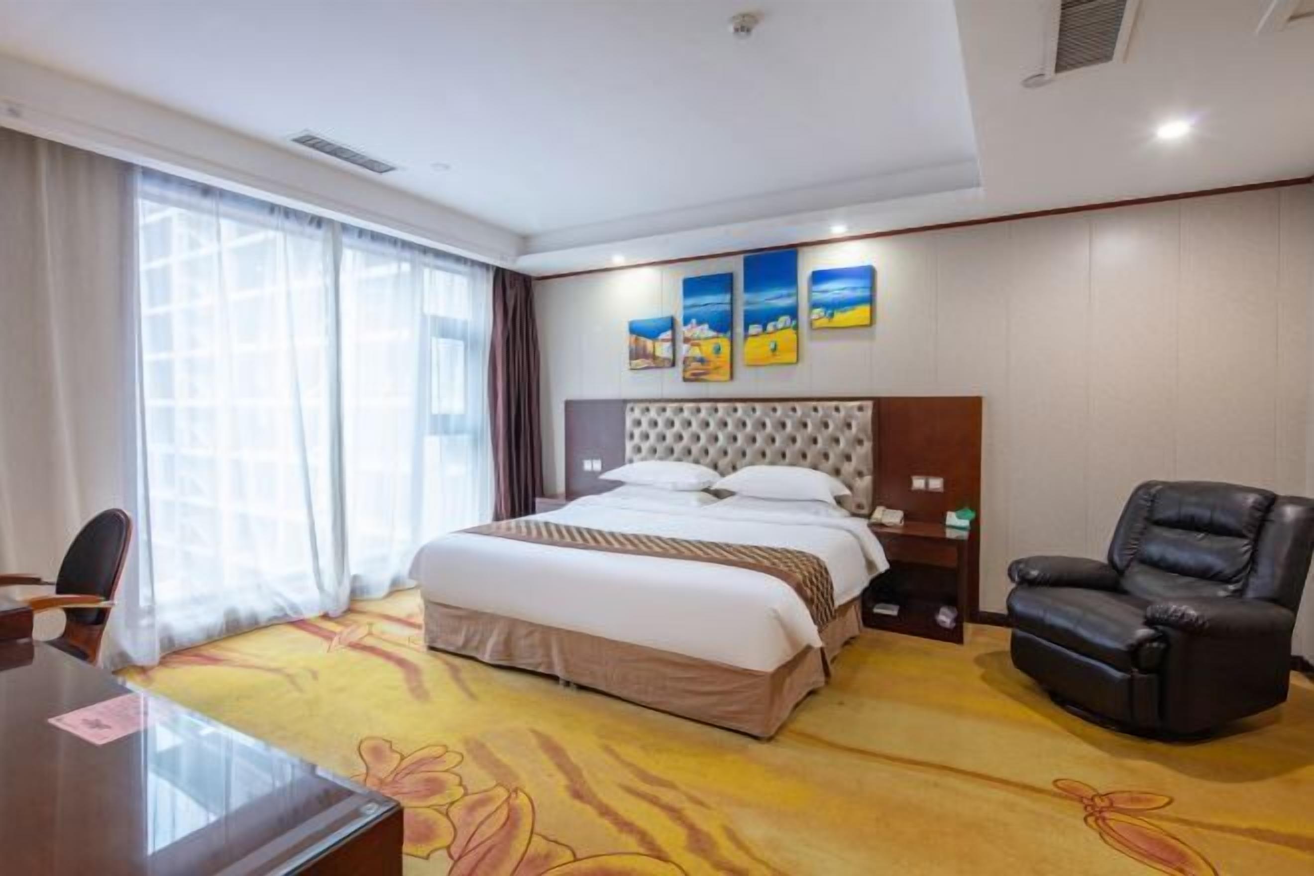 A hotel room with a bed, a desk, a leather chair, and artwork on the wall.