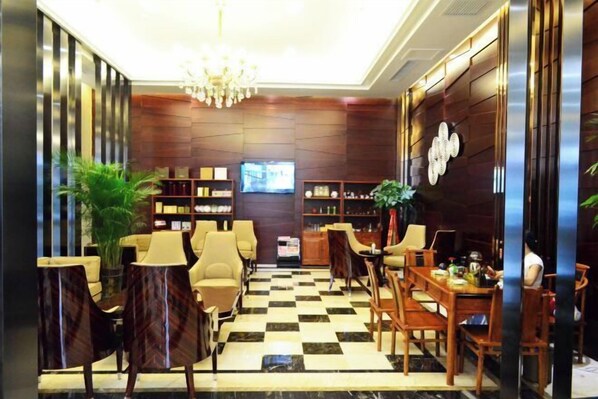 A lobby with a checkered floor, seating area with chairs and tables, a chandelier, and a television on the wall.