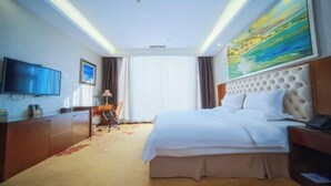 A hotel room with a bed, a television, a desk with a chair, and a painting on the wall. - The BLD International Hotel (Yuncheng)