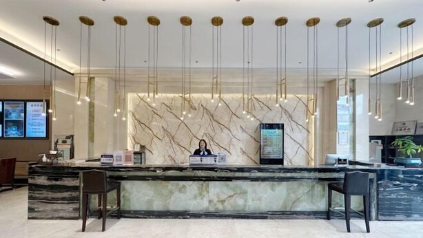A hotel reception area with a marble counter, two chairs, a receptionist, and a digital screen. - The BLD International Hotel (Yuncheng)