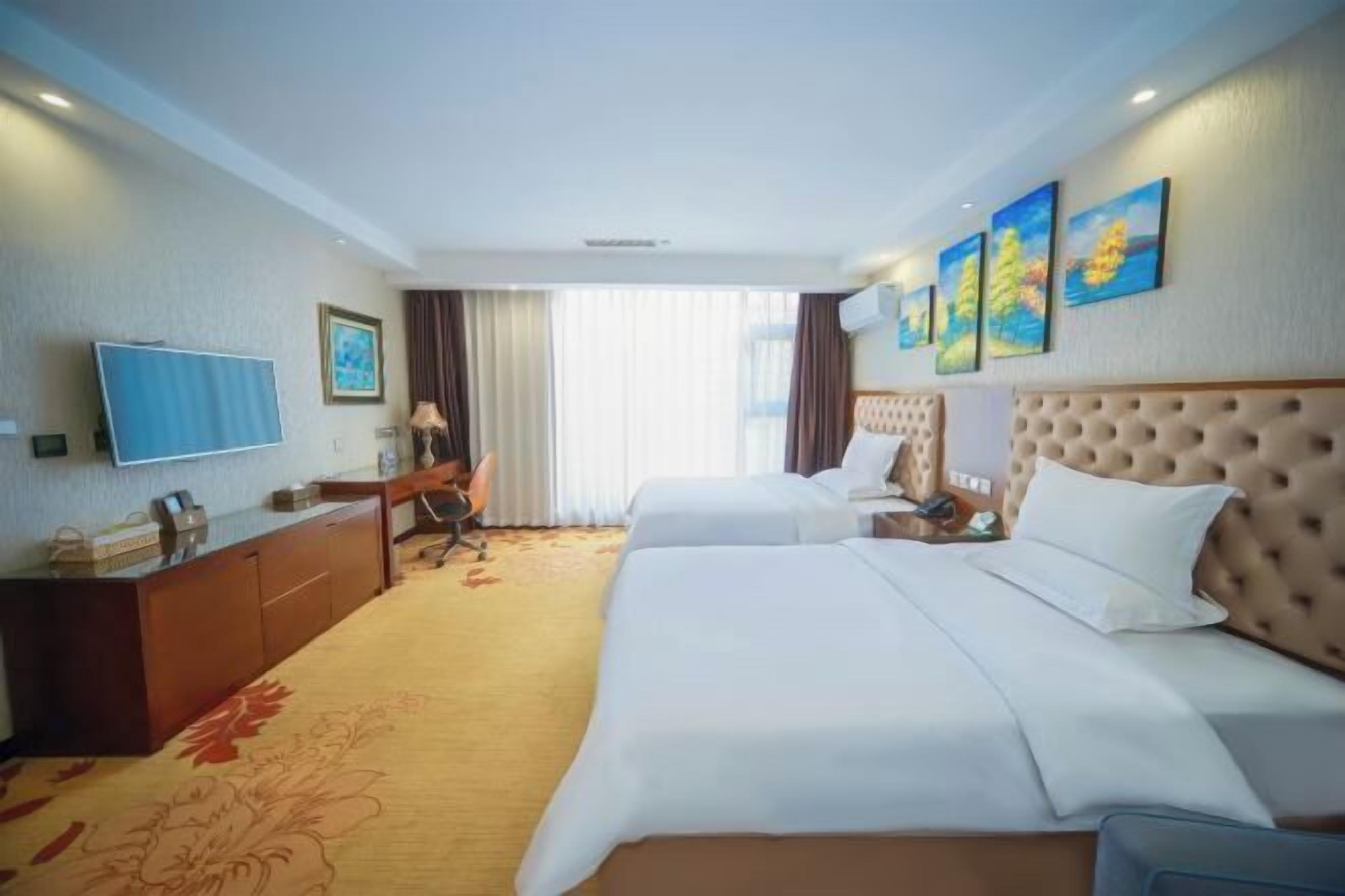 Une chambre d’hôtel avec deux lits, un bureau, une télévision et des œuvres d’art accrochées aux murs.