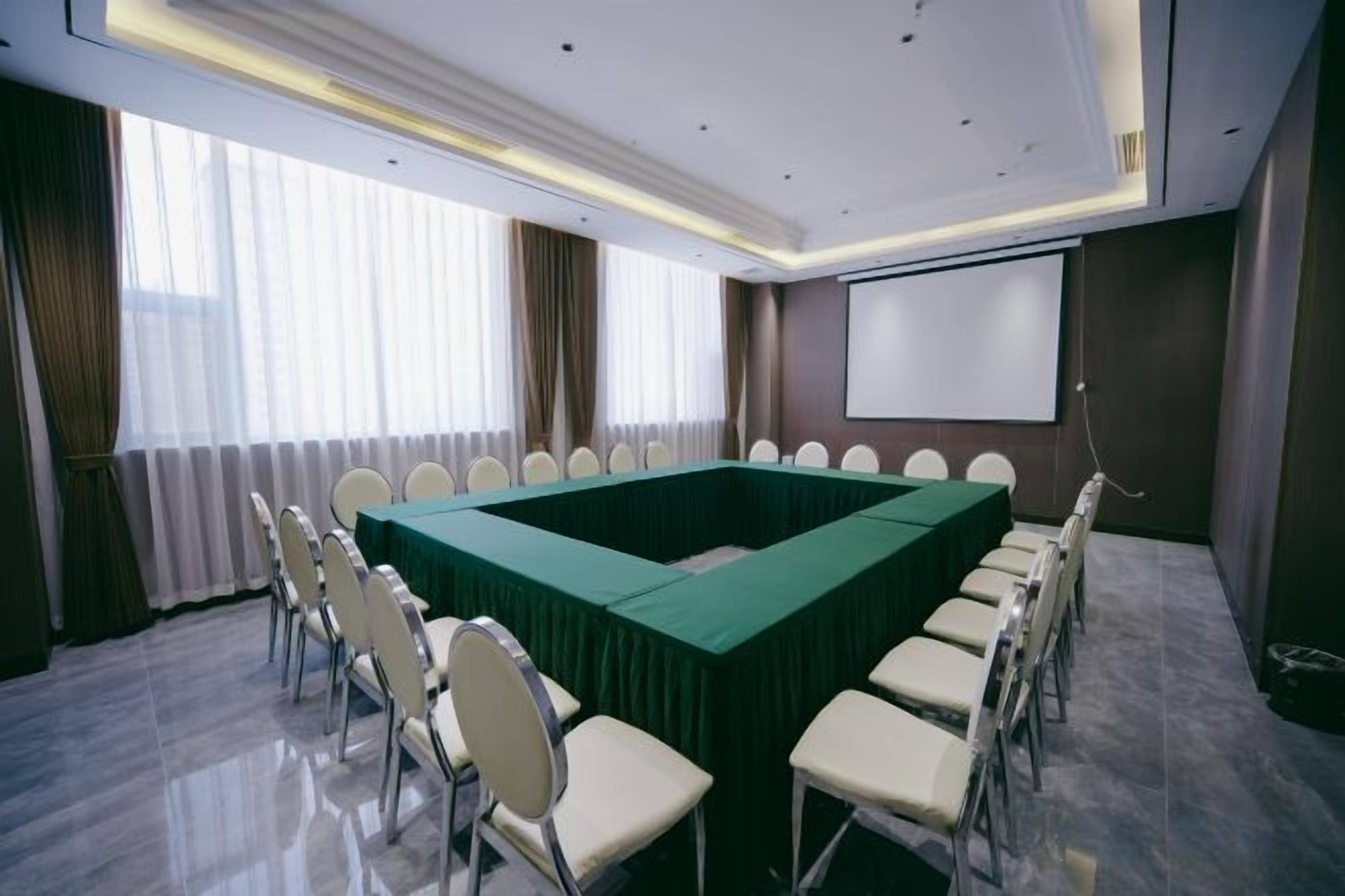 Ein Konferenzraum mit einem langen Tisch, Stühlen, einer Projektionsleinwand und einem großen Fenster mit Vorhängen.
