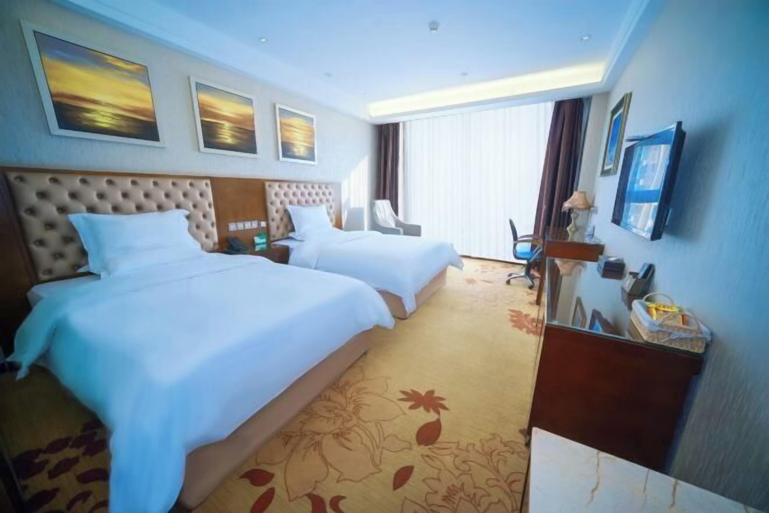 Une chambre d’hôtel avec deux lits, une grande fenêtre et un téléviseur à écran plat.