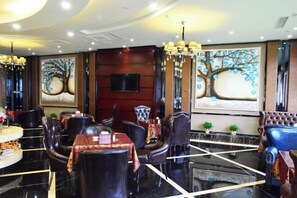 A restaurant with a modern interior, featuring black leather chairs, a central dining table, and artwork depicting trees on the walls.