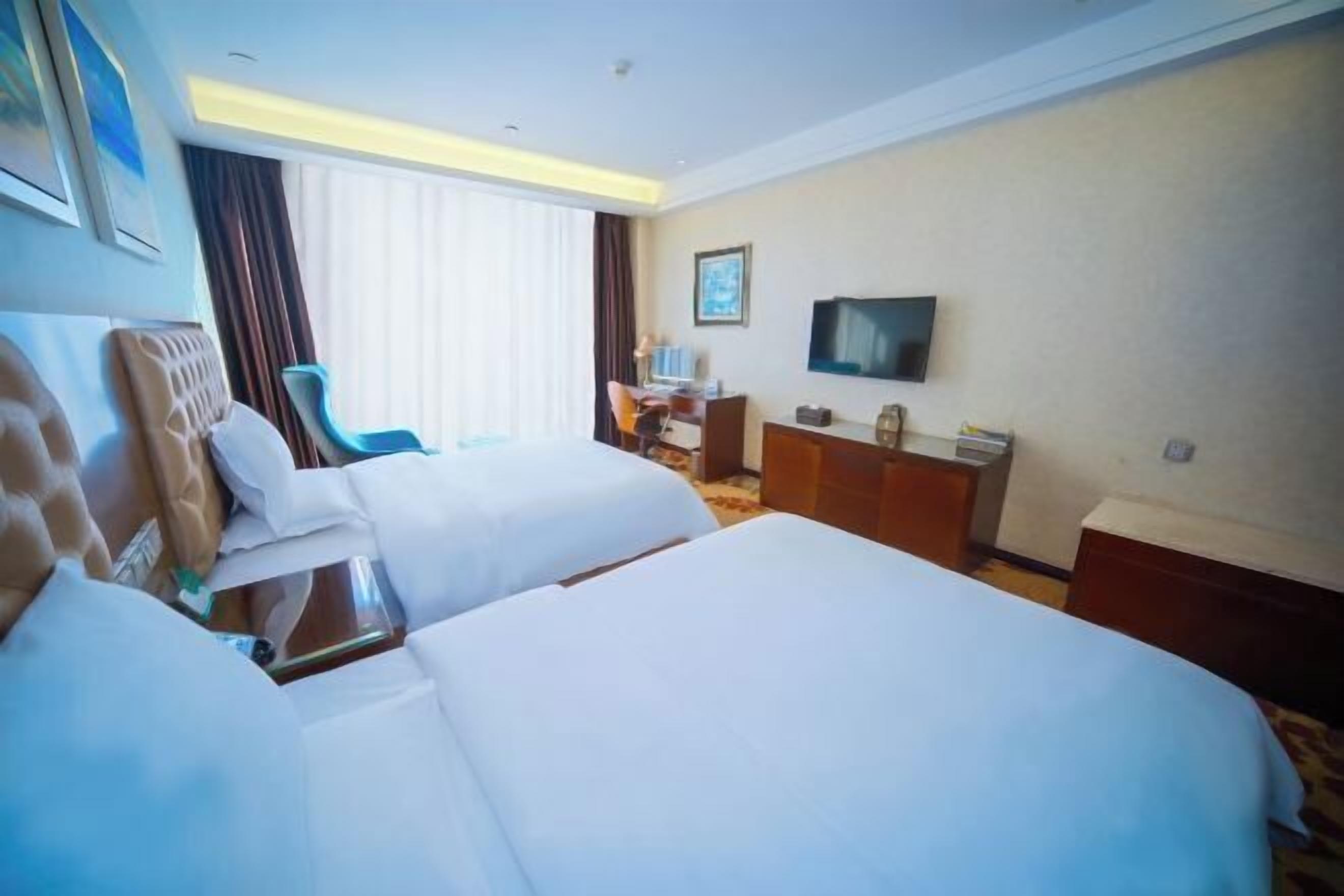 Hotelkamer met twee bedden, een bureau, een stoel, een televisie en een raam met gordijnen.