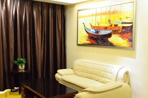 A living room with a beige sofa, a dark wooden coffee table, and a painting of boats on the wall.