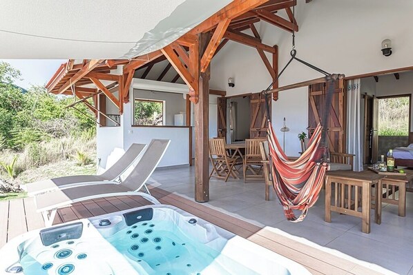 A covered outdoor area with a hot tub, lounge chairs, a dining table, and a hammock.