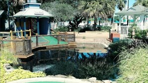Un campo de mini golf con un área de juego verde, un puente de madera y una estructura similar a un pabellón.