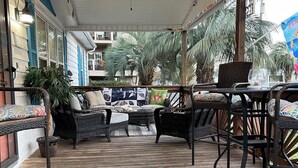 Un área de estar techada al aire libre con muebles de mimbre, un ventilador de techo y un tapete decorativo.