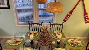 Una mesa de comedor dispuesta para seis personas, con individuales verdes, servilletas a cuadros y una piña como centro de mesa.