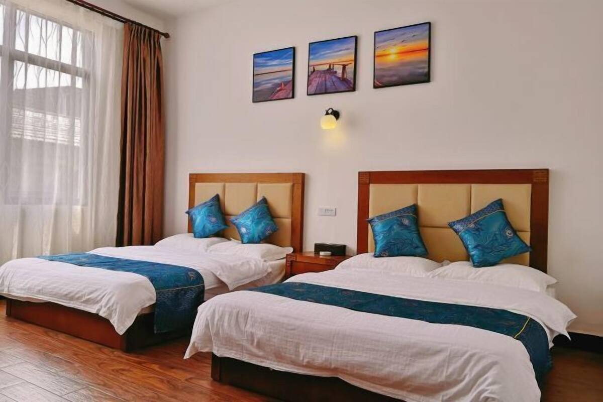 A hotel room with two beds, a wooden headboard, a nightstand, and a wall-mounted lamp.