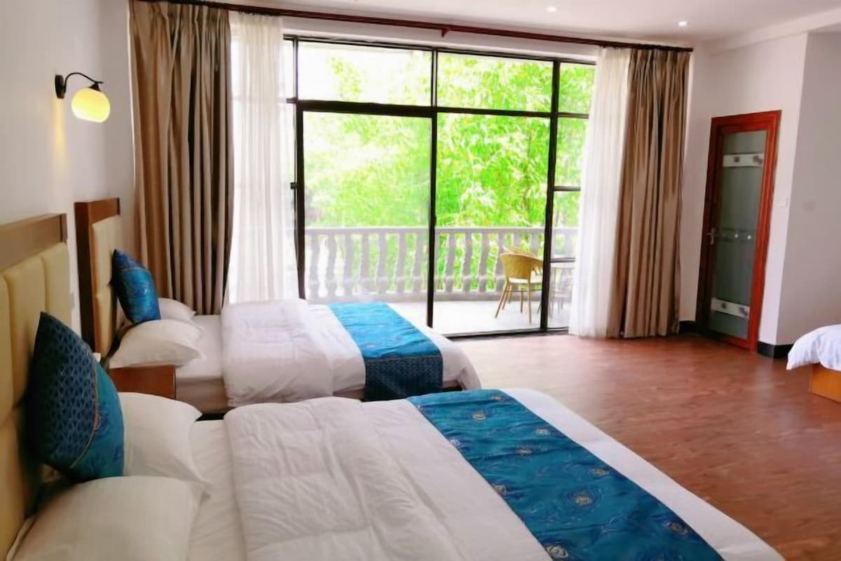 A hotel room with two beds, a balcony, and a sliding glass door to the outside.