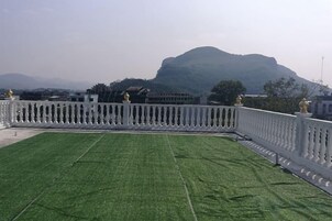 Una terraza en la azotea con césped artificial, barandilla blanca y una montaña al fondo.